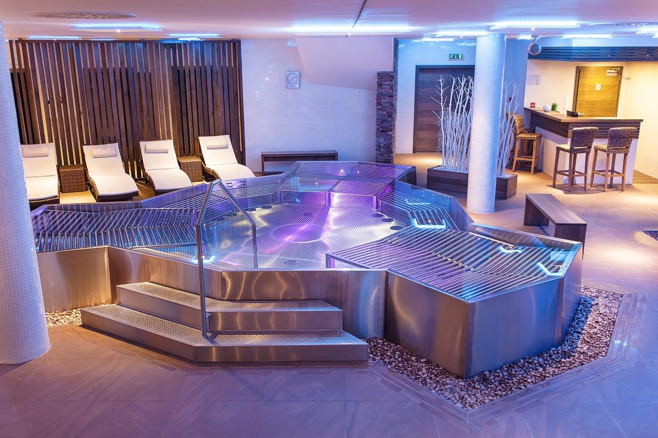 Piscina interior em inox com escadas e iluminação. Referência de espaço wellness.