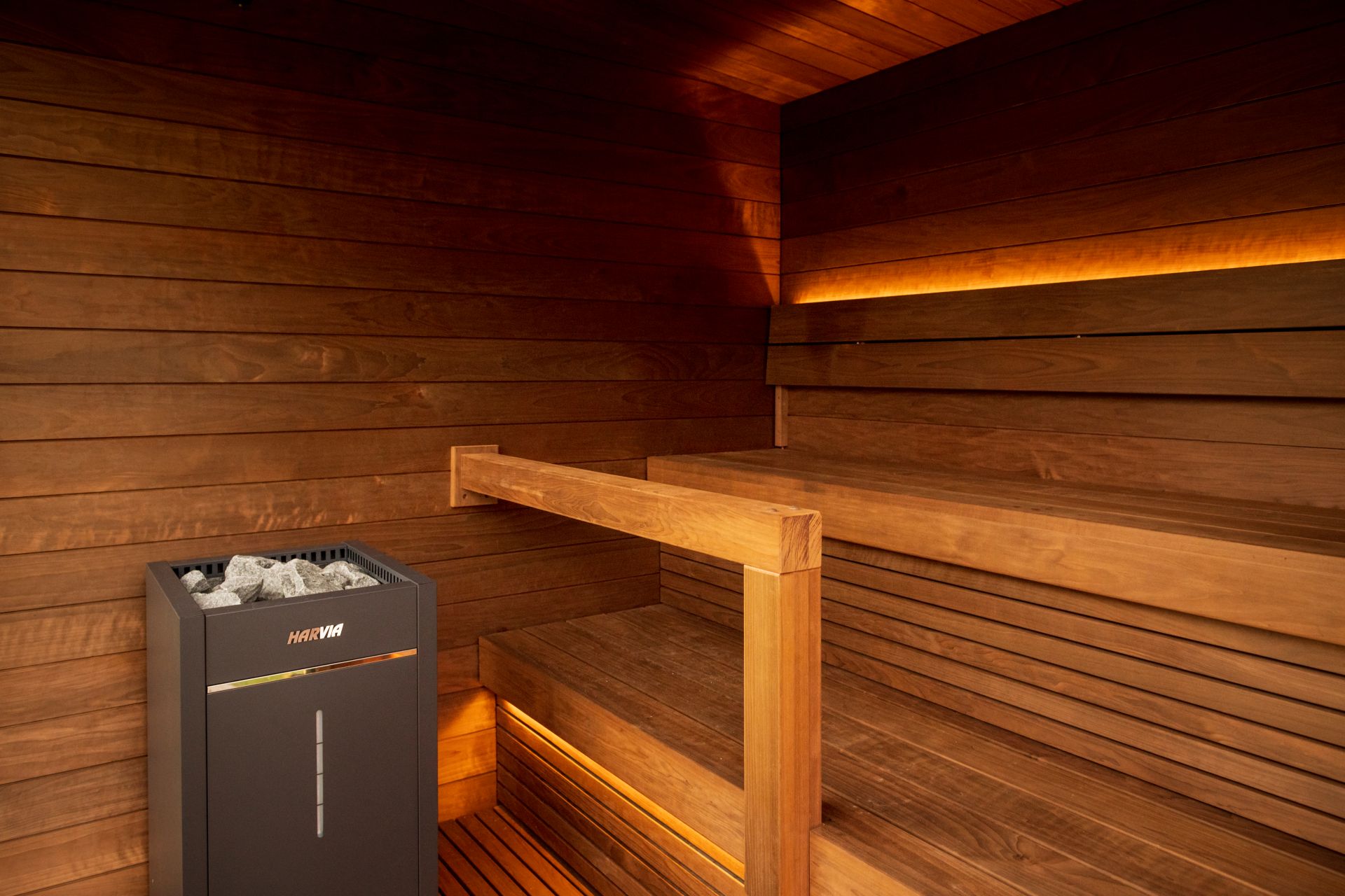 Sauna tradicional em madeira com aquecedor Harvia e iluminação LED indireta, criando um ambiente quente e acolhedor.